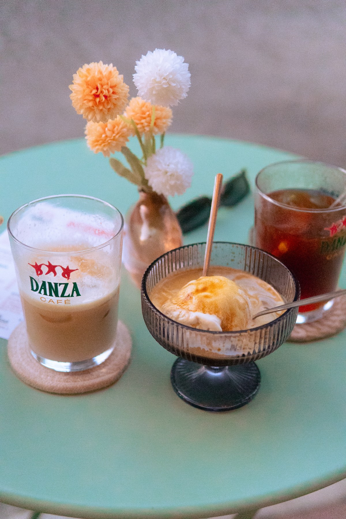 Tabletop still life featuring Danza branded glassware, iced latte on cork coaster, affogato coupe, and cold brew